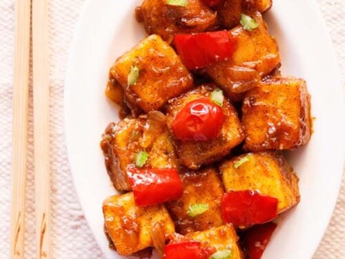 top shot of paneer manchurian on a white platter with bamboo chopsticks by the side.