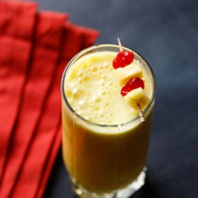 pineapple smoothie recipe garnished with a toothpick of cherries and pineapple chunks.