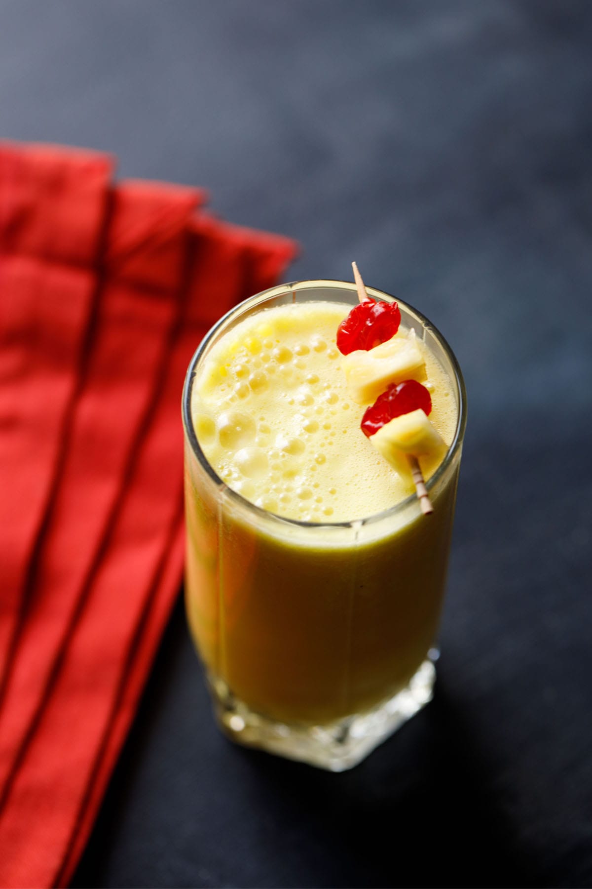 pineapple smoothie recipe garnished with a toothpick of cherries and pineapple chunks.