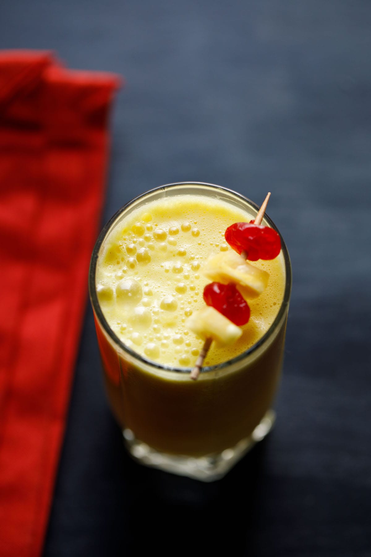 pineapple smoothie recipe garnished with a toothpick of cherries and pineapple chunks.