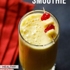 pineapple smoothie in a glass garnished with a toothpick of cherries and pineapple chunks with text layovers