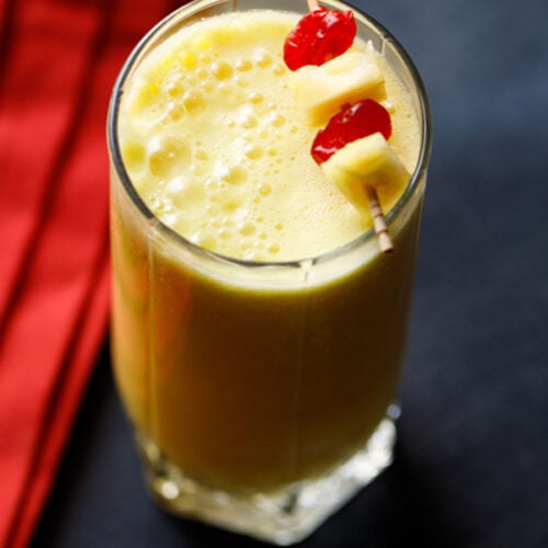 pineapple smoothie recipe garnished with a toothpick of cherries and pineapple chunks.
