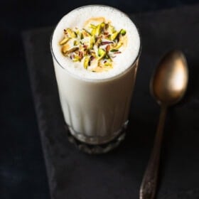 vanilla milkshake served in a glass. topped with chopped pistachios.