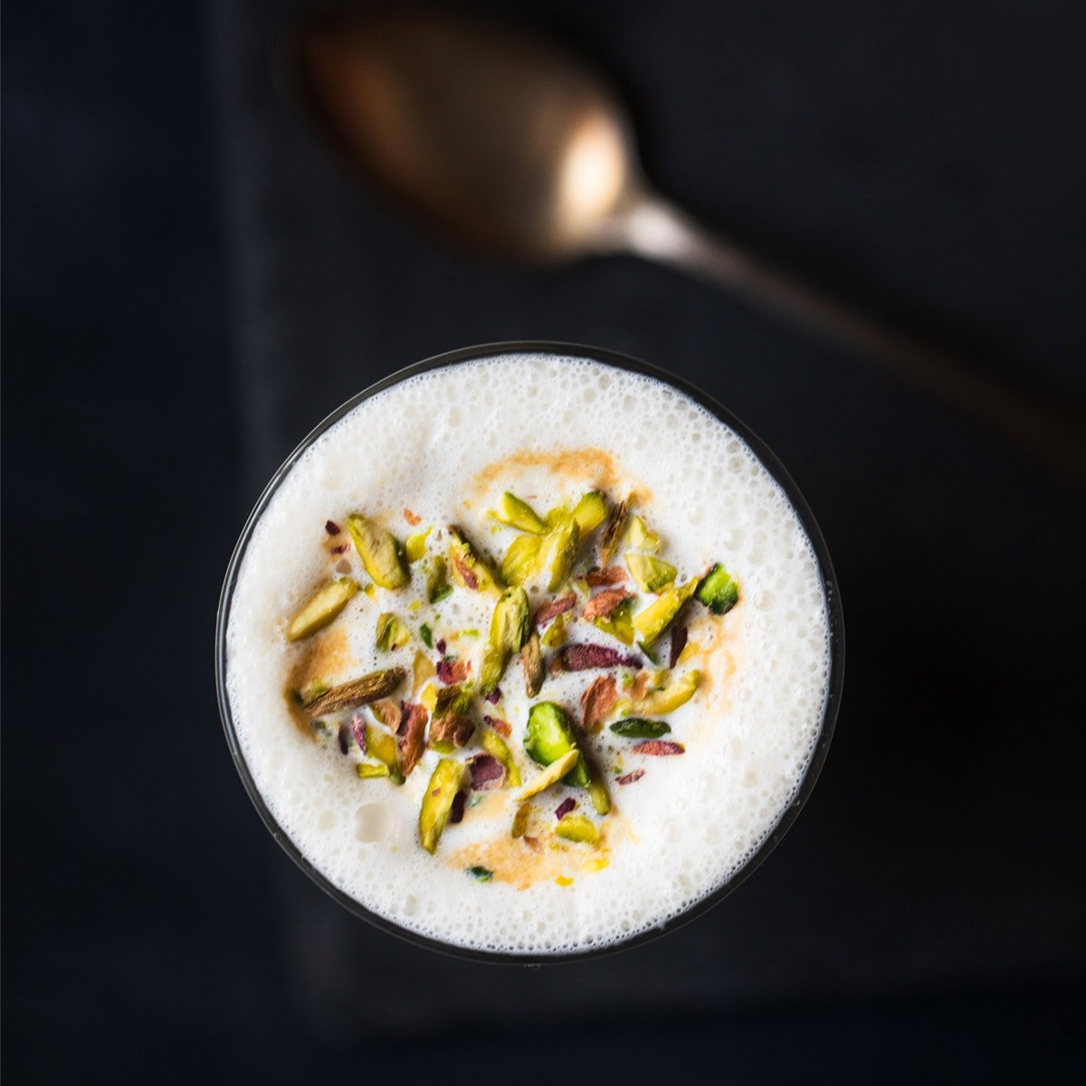 vanilla milkshake served in a glass. topped with chopped pistachios.