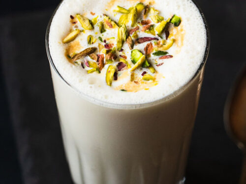 vanilla milkshake served in a glass. topped with chopped pistachios.
