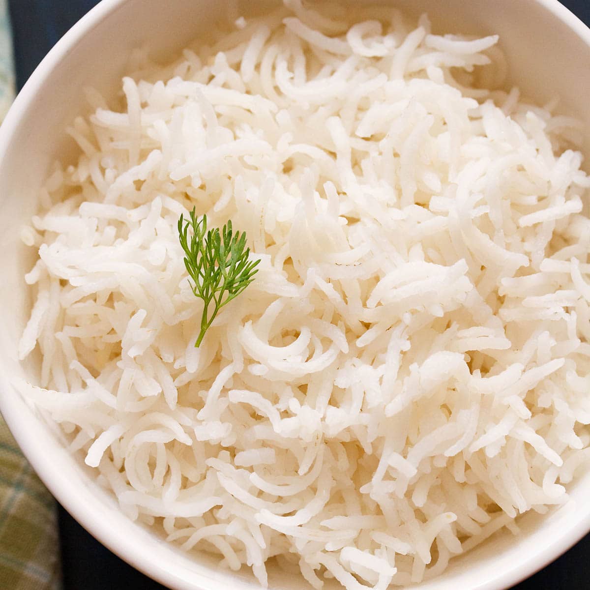 cooked basmati rice in a white bowl with a coriander sprig on top.