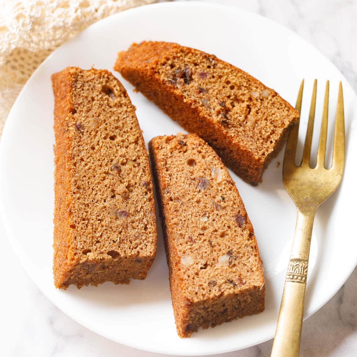 three date cake slices on white plate with golden fork by the side.