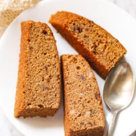 three date cake slices on white plate with dessert brass spoon.