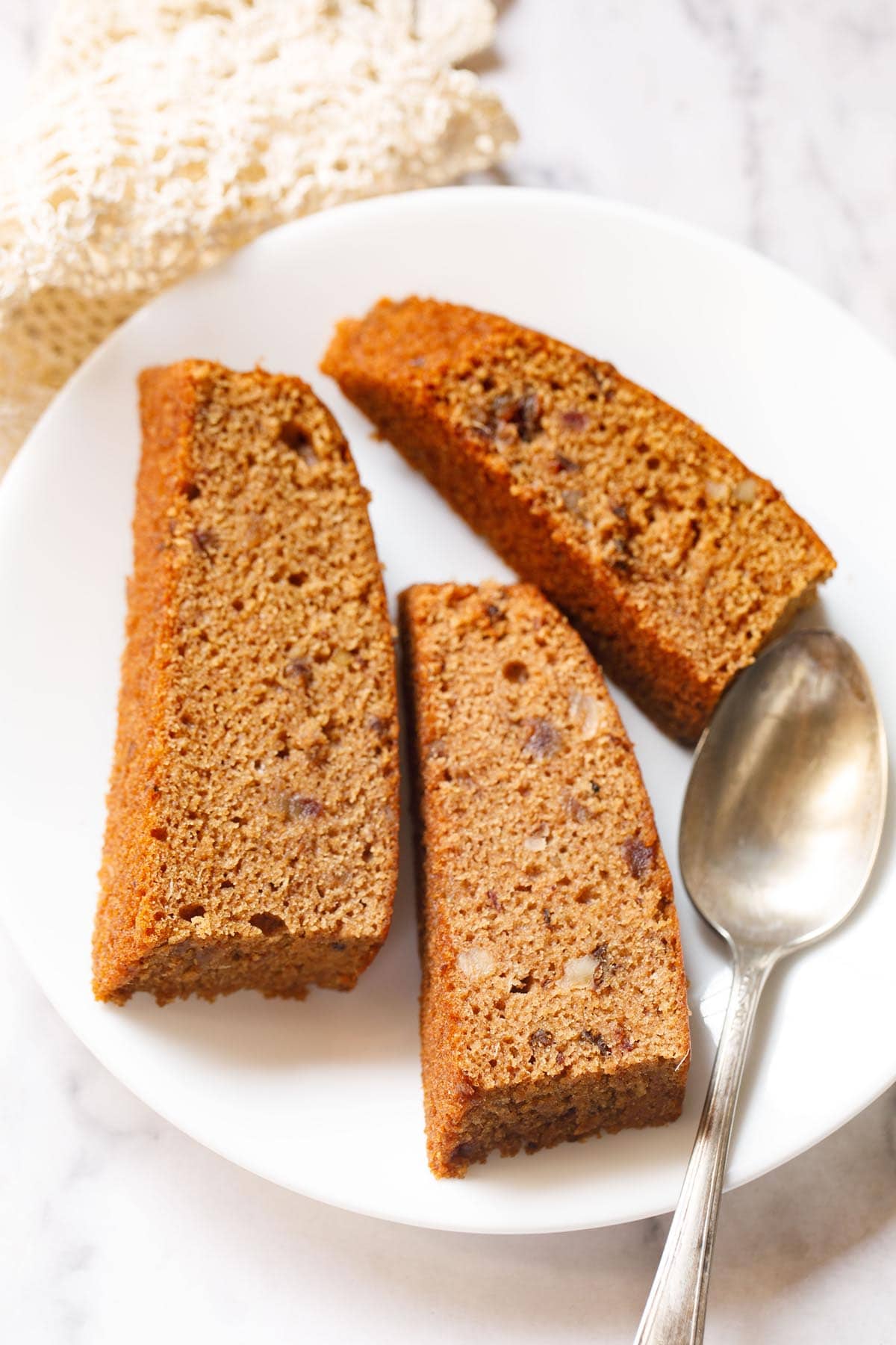 three date cake slices on white plate with dessert brass spoon.