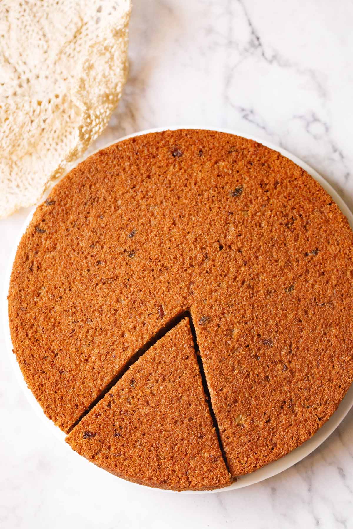 date walnut cake on white plate with cream colored doily on top.