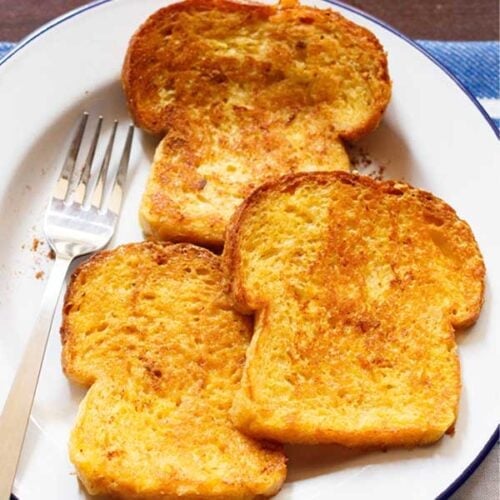 three french toast served on a white plate with a fork by the side.