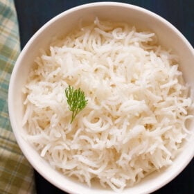 cooked basmati rice in a white bowl with a coriander sprig on top.