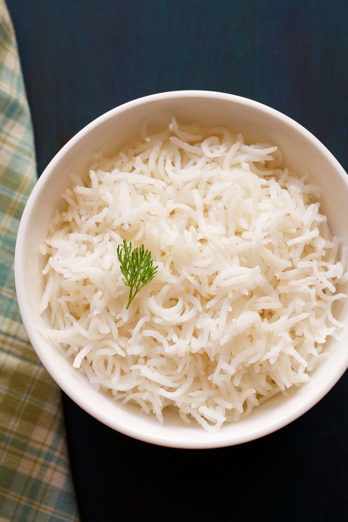 cooked basmati rice in a white bowl with a coriander sprig on top.