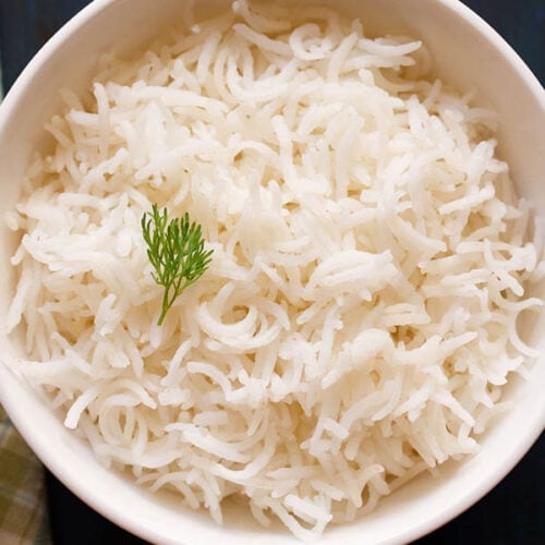 cooked basmati rice in a white bowl with a coriander sprig on top.