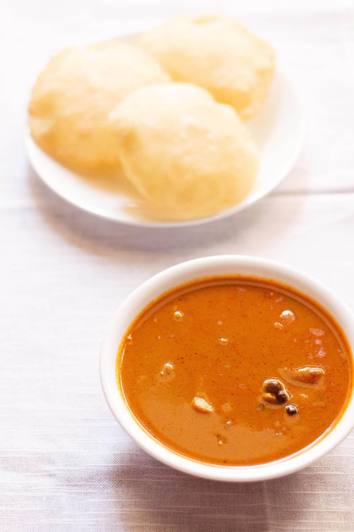 kala vatana sambar in bowl with a plate of rice pooris placed on top.