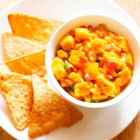 mango salsa served in a bowl with tortilla chips on a plate.