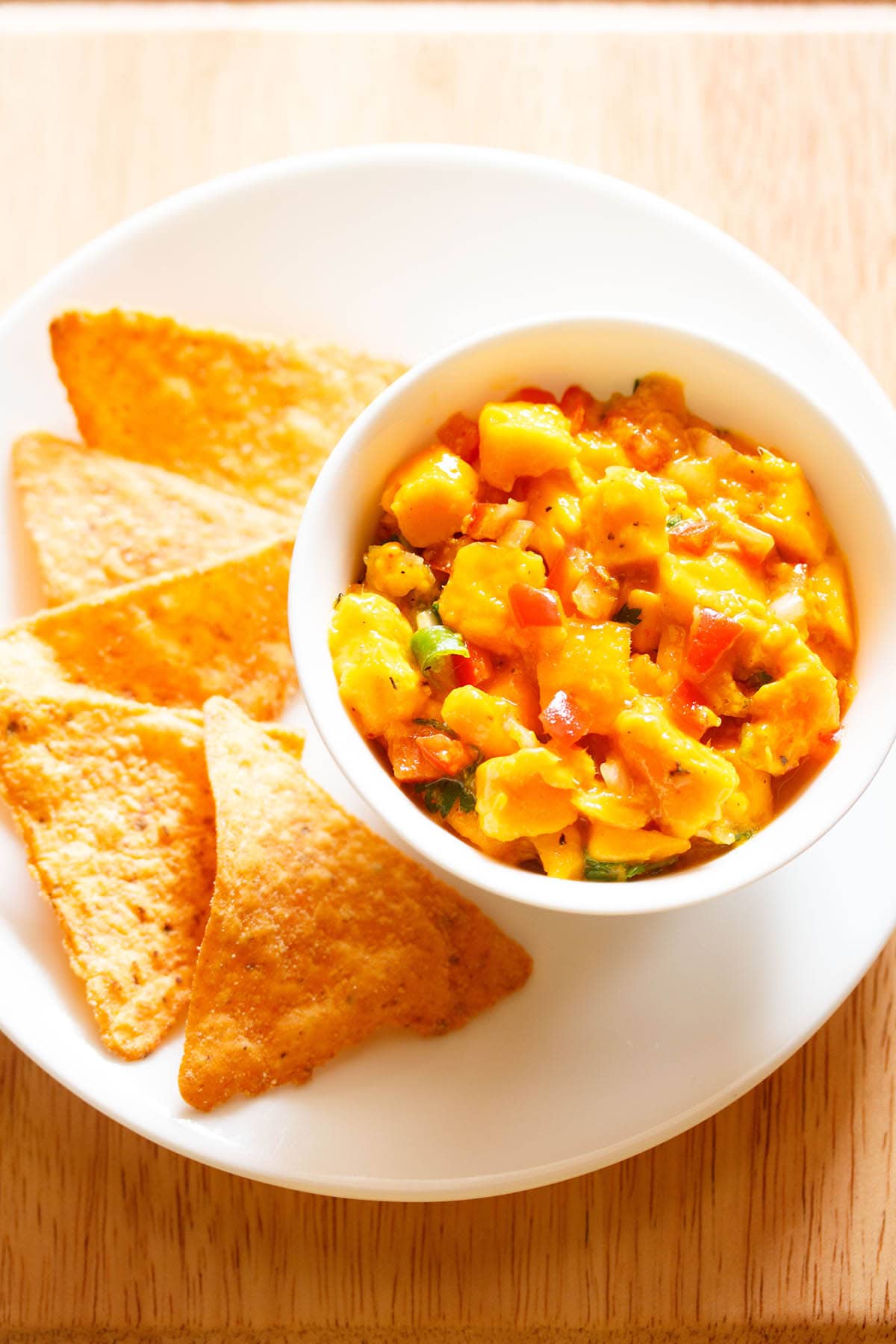 mango salsa served in a bowl with tortilla chips on a plate.