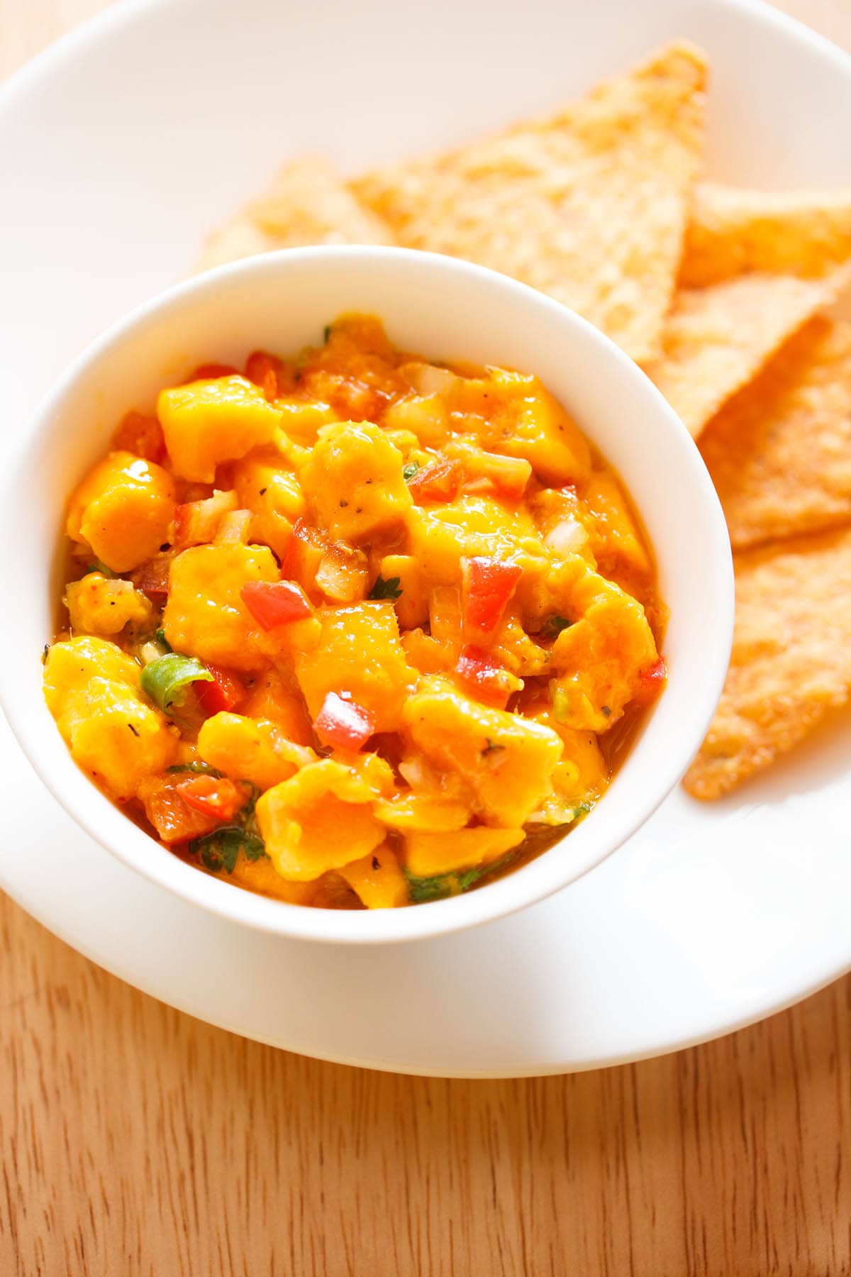 mango salsa served in a bowl with tortilla chips on a plate.