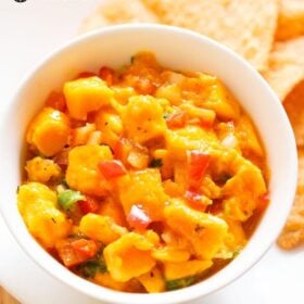 closeup shot of mango salsa served in a bowl with tortilla chips on a plate with text layovers.