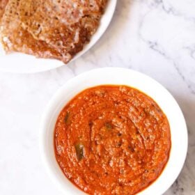 overhead shot of tomato pickle or tomato thokku in white bowl with text layovers.