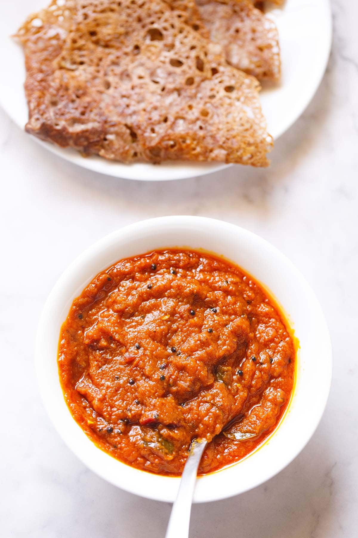 tomato thokku in white bowl with a spoon inside.