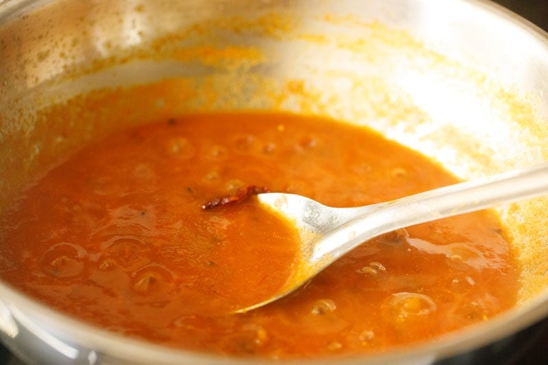 simmering tomato pickle in pan with a spoon inside.