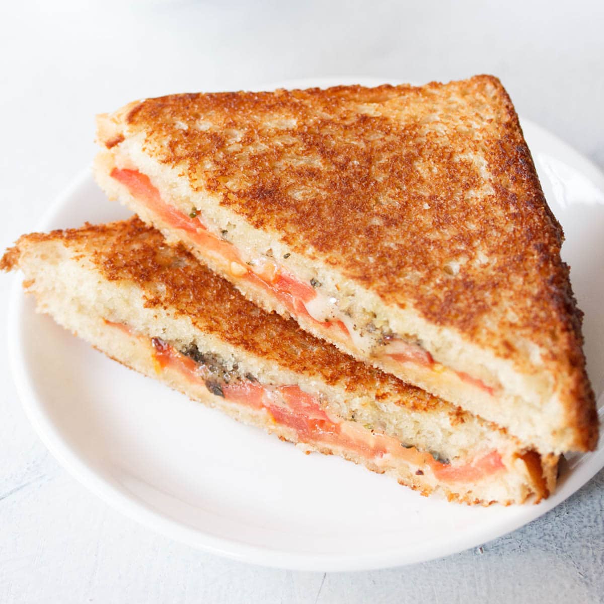 cheese and tomato sandwich served on a white plate on a white table.