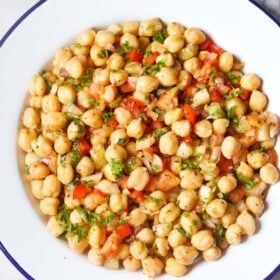 chickpea salad in a white plate with a blue rim on a marble table.