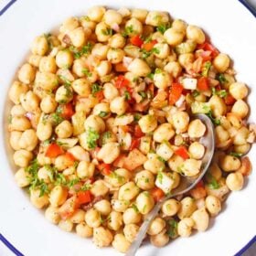 chickpea salad in a blue rimmed white plate with a spoon on a marble table with text layovers.