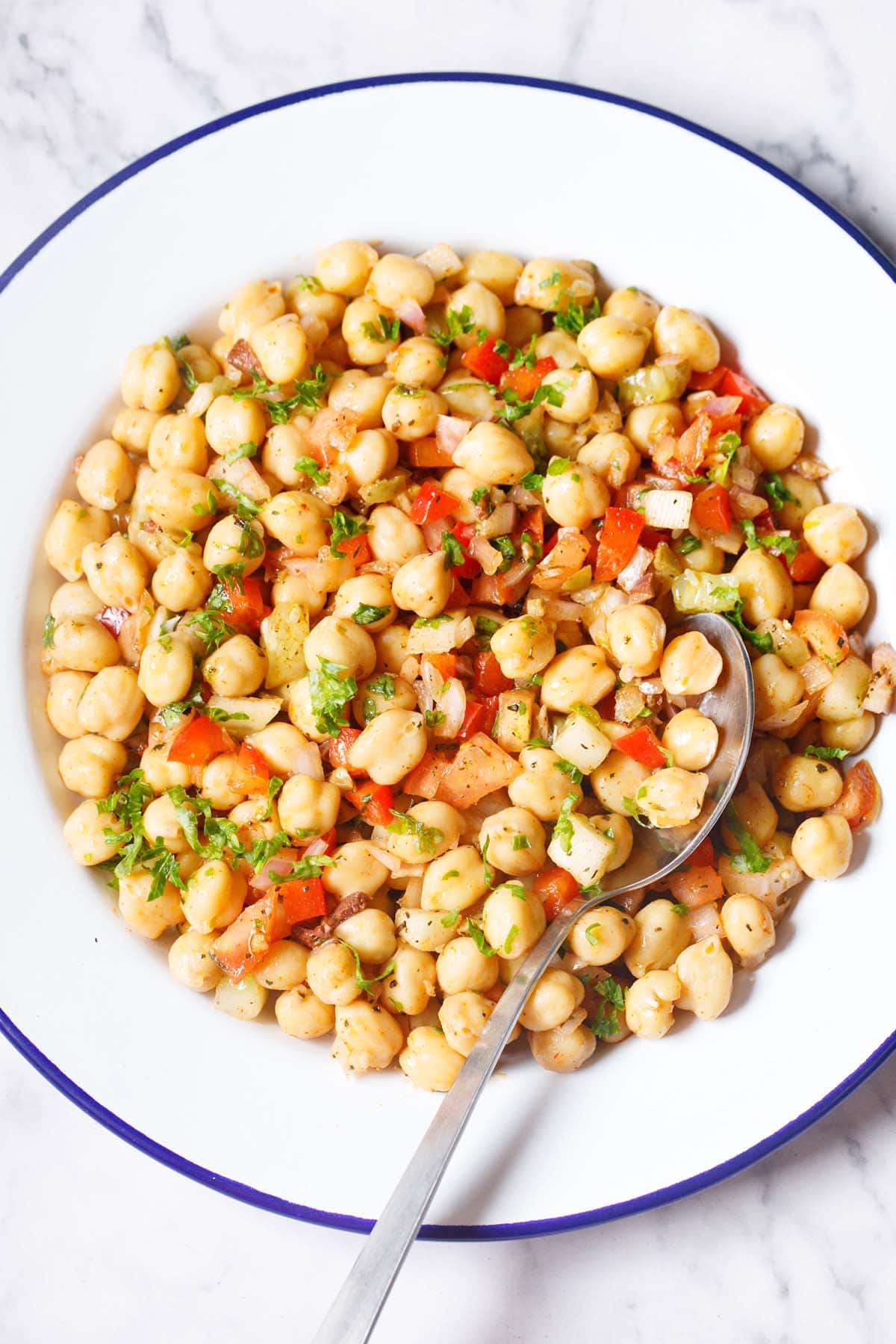 chickpea salad in a blue rimmed white plate with a spoon on a marble table.