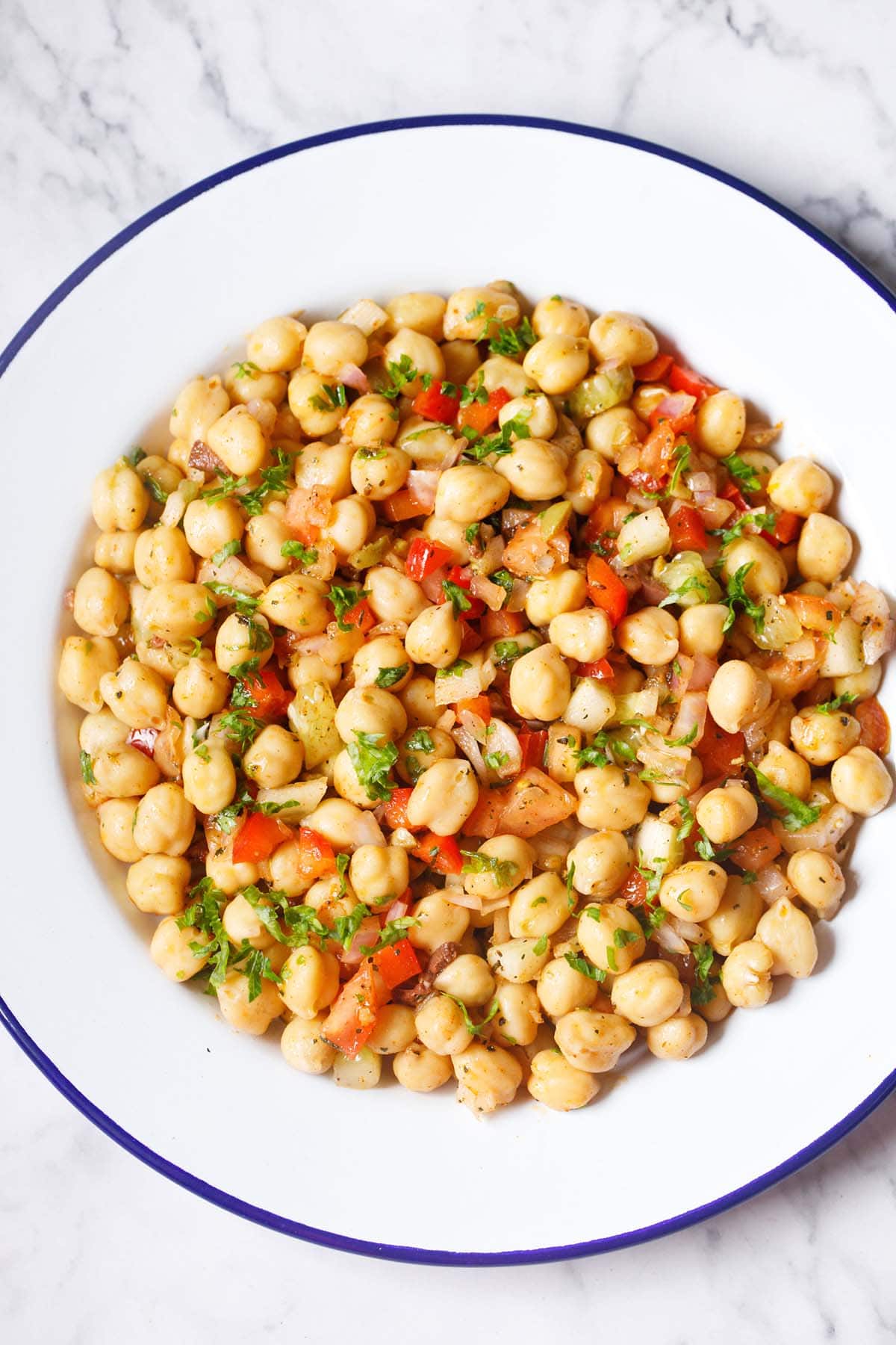 chickpea salad in a white plate with a blue rim on a marble table.