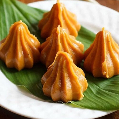 mawa modak served on a fresh turmeric leaf kept on a white plate.