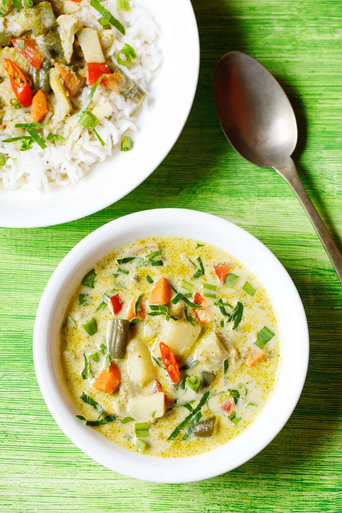 thai green curry in a white bowl with a plate of green curry and rice and a spoon at the top