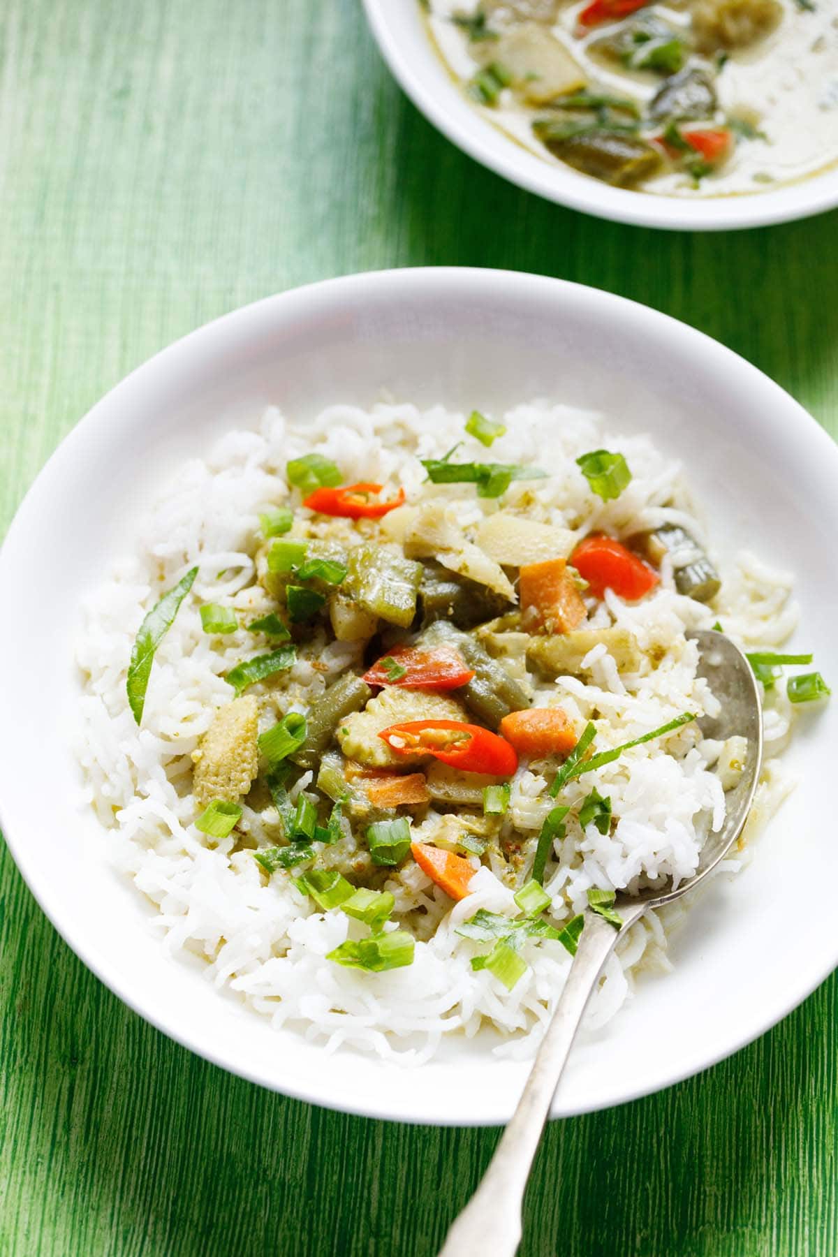 thai green curry served on a bed of steamed white rice on a white plate with a spoon.