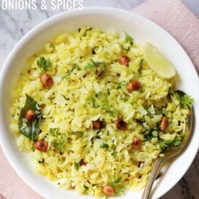poha or pohe in a white bowl with a lemon wedge and spoon.