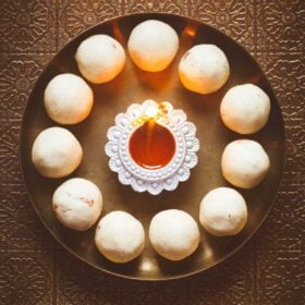 Rava laddoos in a circle with a lighted earthen lamp in the center of a bronze plate.