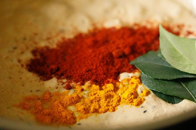 coconut-spice masala paste added to pan with turmeric and cumin for preparing bagara baingan recipe.