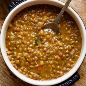 brown lentils or whole masoor dal in bowl with spoon inside the lentils.