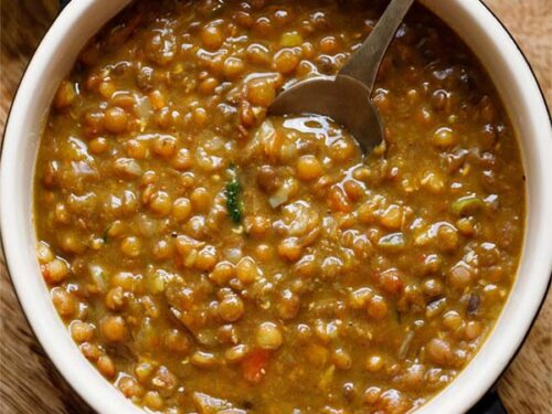brown lentils or whole masoor dal in bowl with spoon inside the lentils.