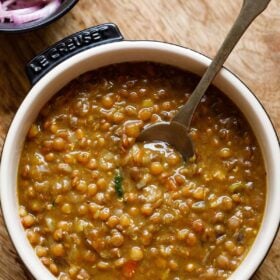 brown lentils or whole masoor dal in bowl with spoon inside the lentils.