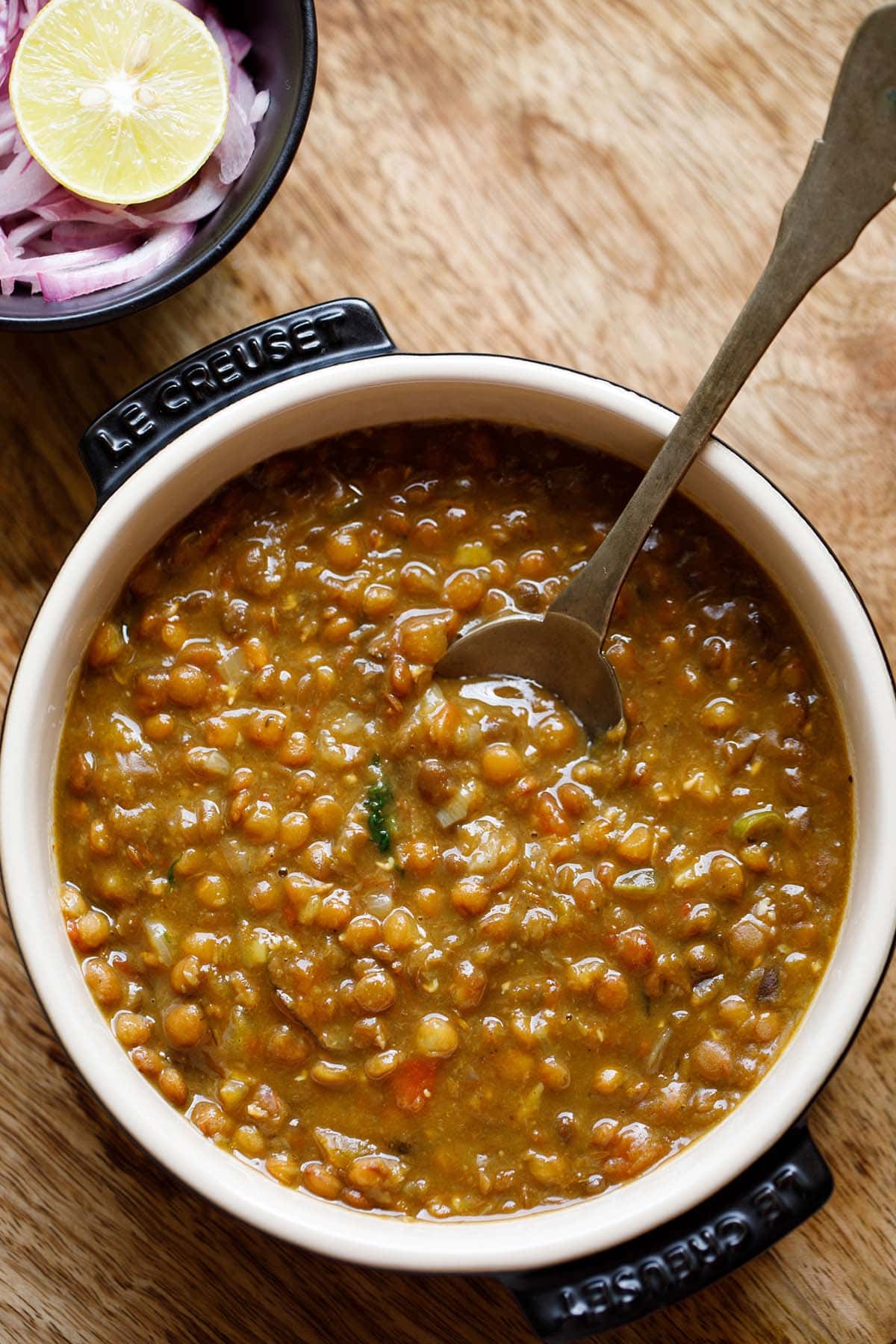 brown lentils or whole masoor dal in bowl with spoon inside the lentils.