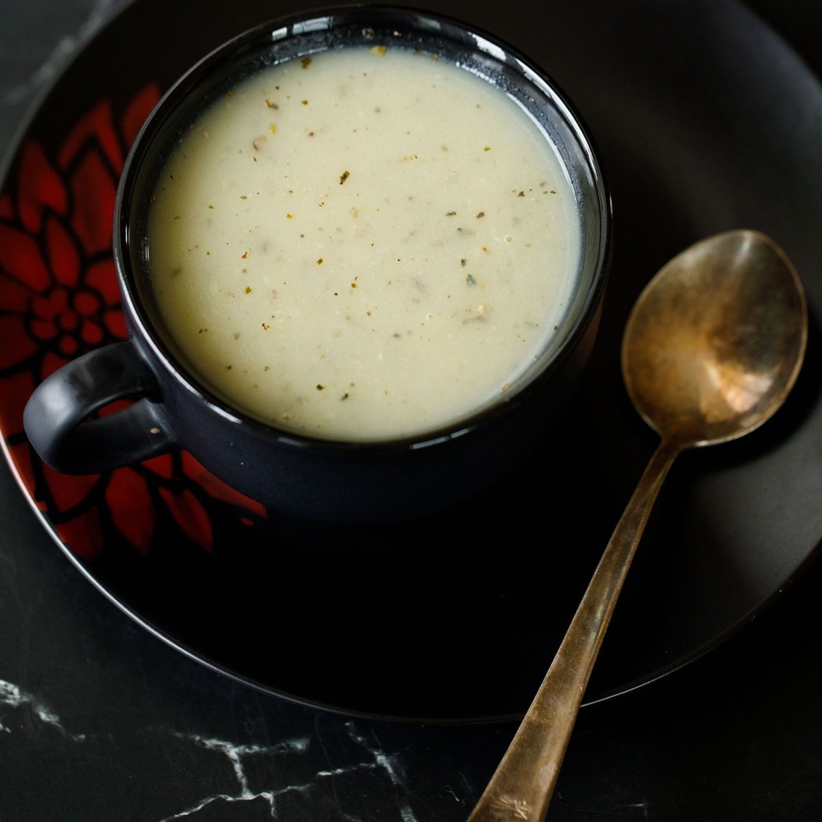 calabash soup or bottle gourd soup in black soup on black plate with a brass spoon by the side.