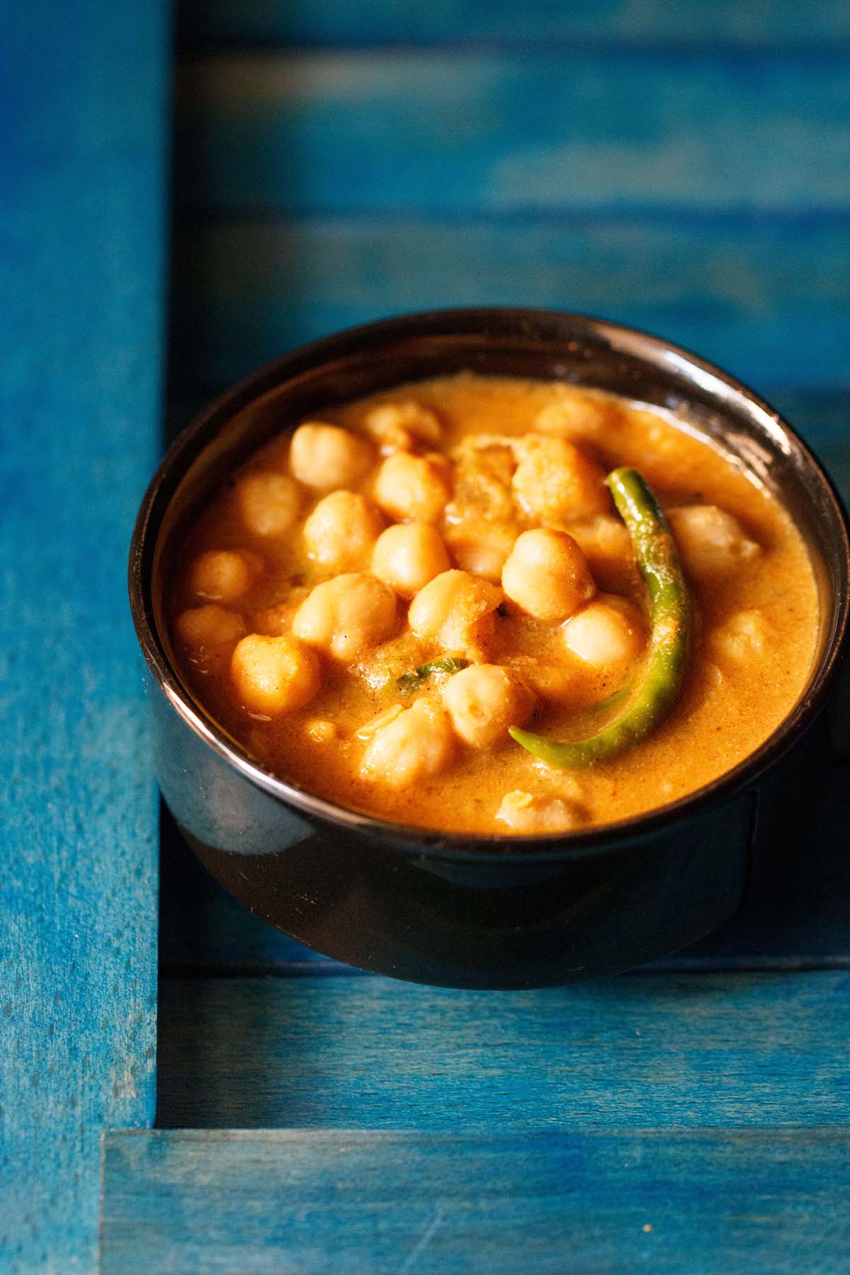chickpea curry in black bowl on a blue wooden tray.