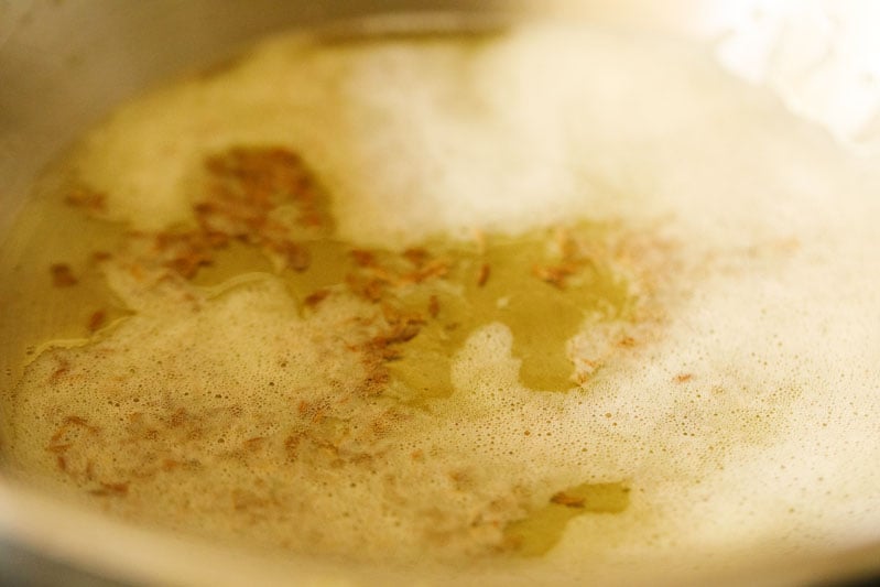 frying cumin seeds in hot ghee in a pan. 