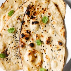 closeup shot of three garlic naan with mint leaves garnish.