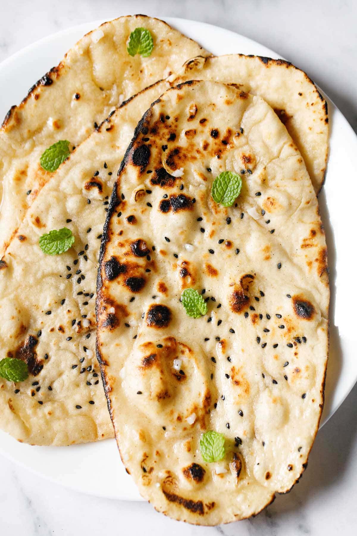 closeup shot of three garlic naan with mint leaves garnish.