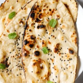 closeup shot of three garlic naan with mint leaves garnish.