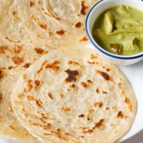 kerala parotta on white plate with a bowl of green curry at top right.