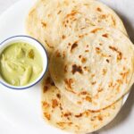 kerala parotta placed on white plate with a bowl of green curry at left side.