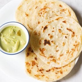 kerala parotta placed on white plate with a bowl of green curry at left side.